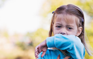 young girl coughing into her elbow