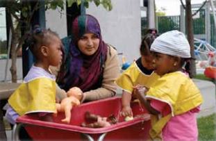 Teacher is nearby, carefully watching three children play in the water table.