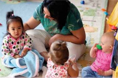 Teacher sits on floor with three infants.