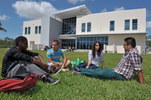 Photo of students sitting in the grass outside a building.